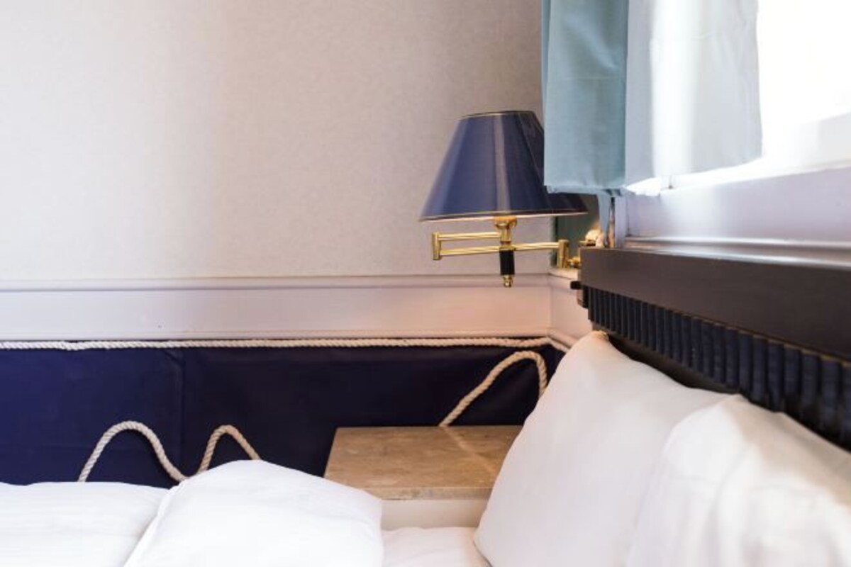 A neatly made bed with white bedding, a dark blue headboard, and a bedside table with a lamp.