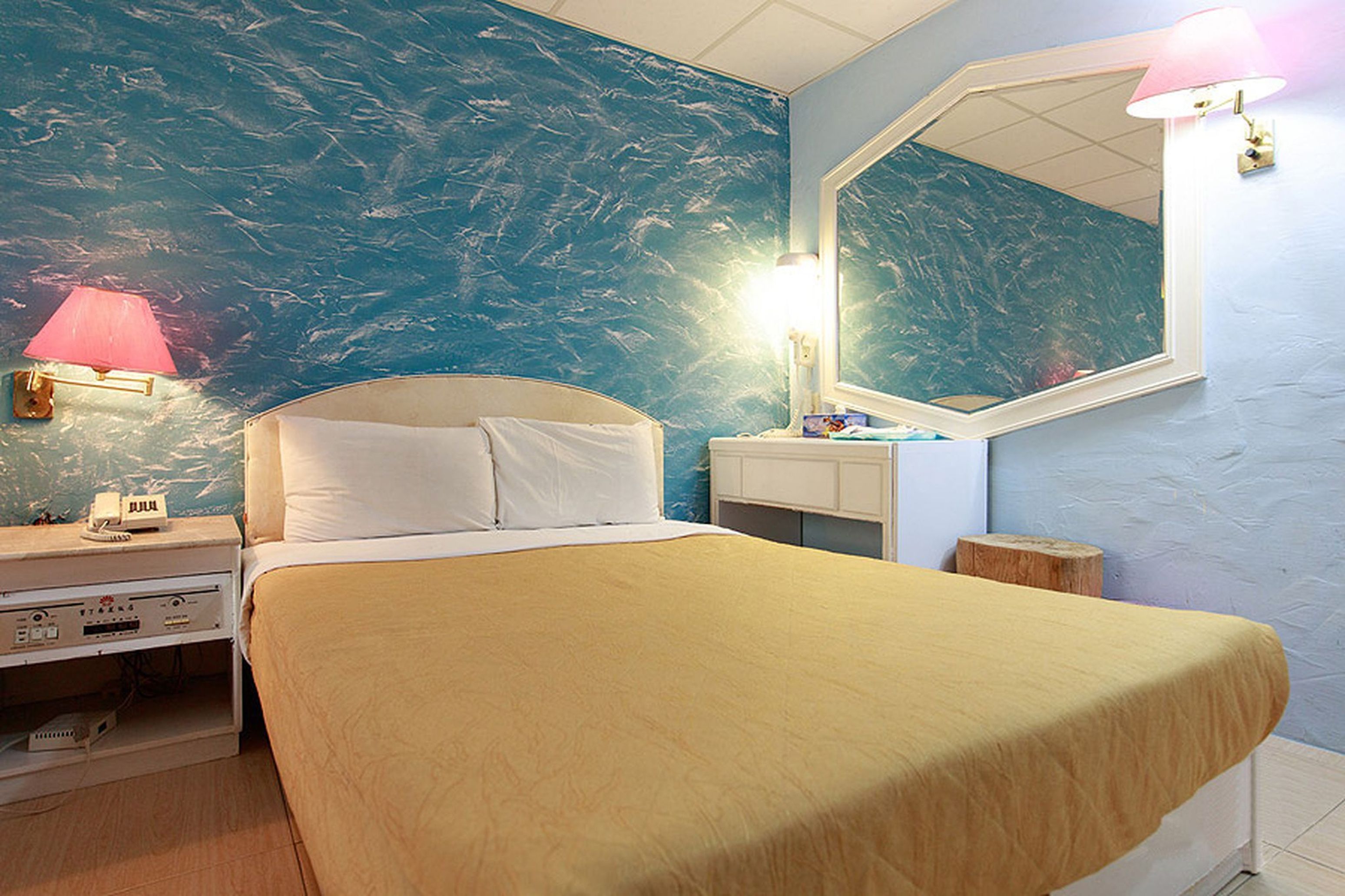 Un dormitorio con cama, una mesita de noche con lámpara, un espejo y un aparador.