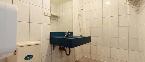 Un baño pequeño con paredes de azulejos blancos, un inodoro blanco, un lavamanos azul y una zona de ducha.
