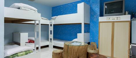 A room with bunk beds, a television, wooden stools, and a cabinet.