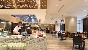 A modern restaurant with marble countertops, a chef preparing food, and a dining area with tables and chairs. - Pullman Yangon Centrepoint (Yangon)
