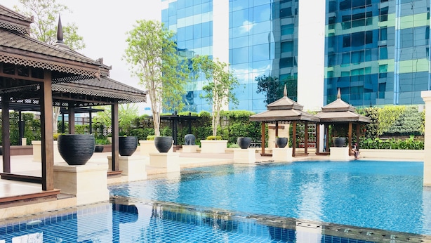 A swimming pool with tiled flooring, surrounded by pavilions and large planters, with modern buildings in the background. - Pullman Yangon Centrepoint (Yangon)