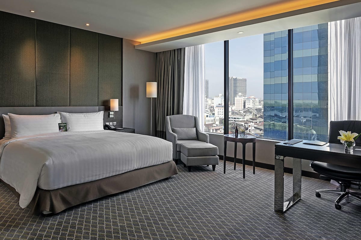 Ein Hotelzimmer mit einem großen Bett, einem Schreibtisch mit Stuhl, Blick auf die Stadt und einem modernen Design.