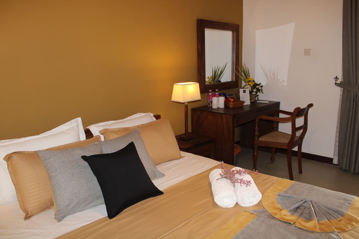 Ett hotellrum med en säng, ett skrivbord, en stol, en lampa och en spegel.