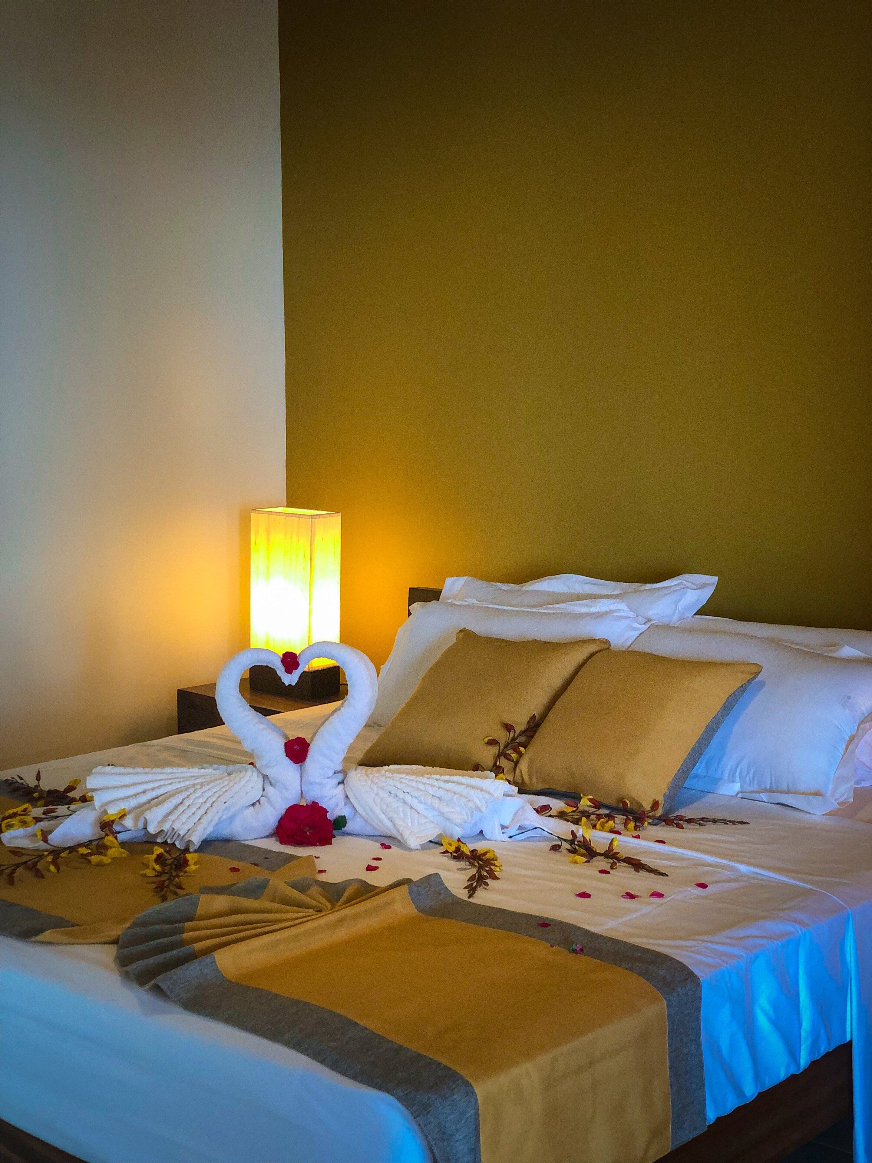 A hotel room with a neatly made bed, a decorative swan towel, and a warm-toned wall.