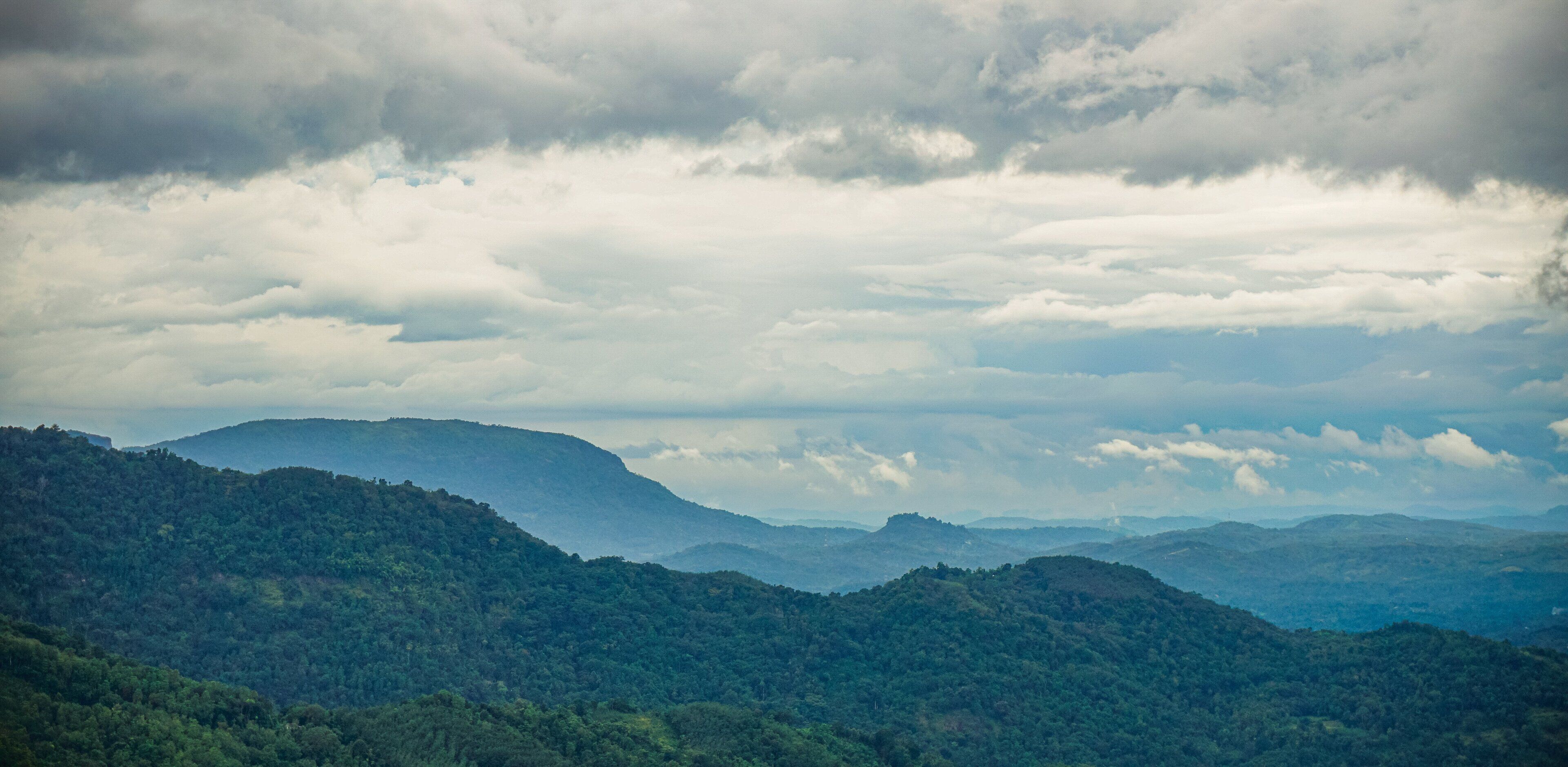 A mountainous landscape with dense forest coverage and a cloudy sky.