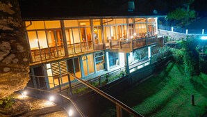 A multi-story building with balconies, a stone wall, and a well-lit outdoor area. - Misty Hills Villa Kadugannawa (Udunuwara)