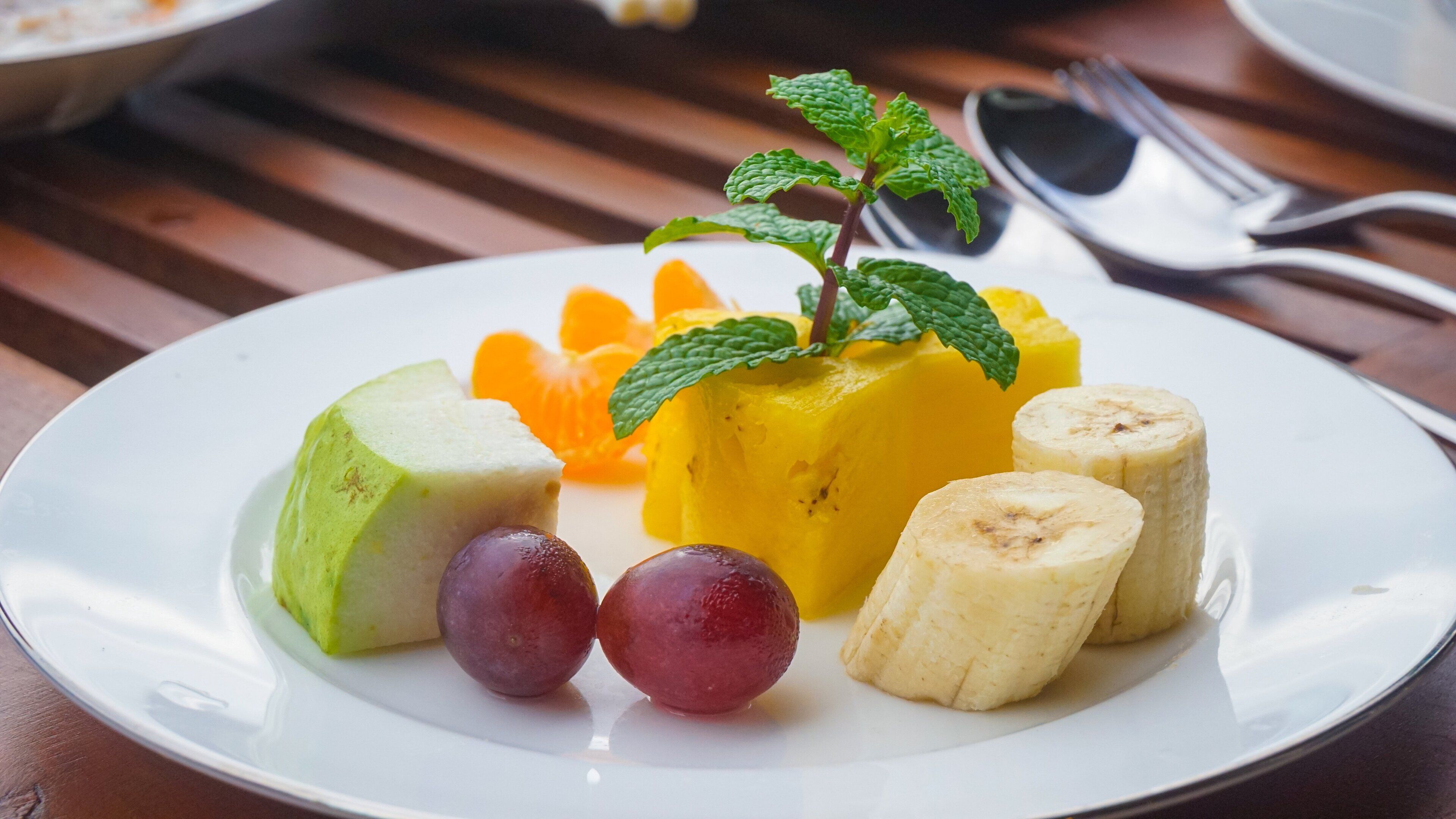 A plate with a yellow fruit, green fruit, bananas, and grapes.