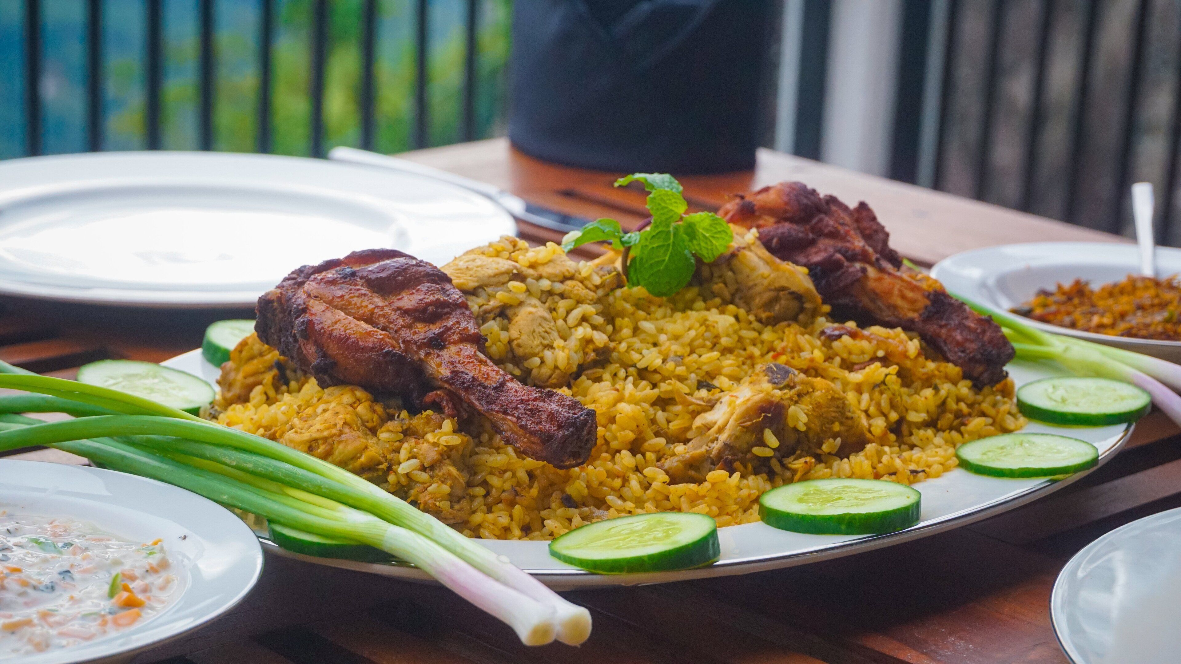 Un piatto di biryani con pollo e fette di cetriolo su un tavolo di legno.