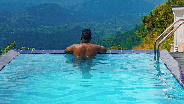 A person in a swimming pool with a view of mountains and cloudy sky. - Misty Hills Villa Kadugannawa (Udunuwara)
