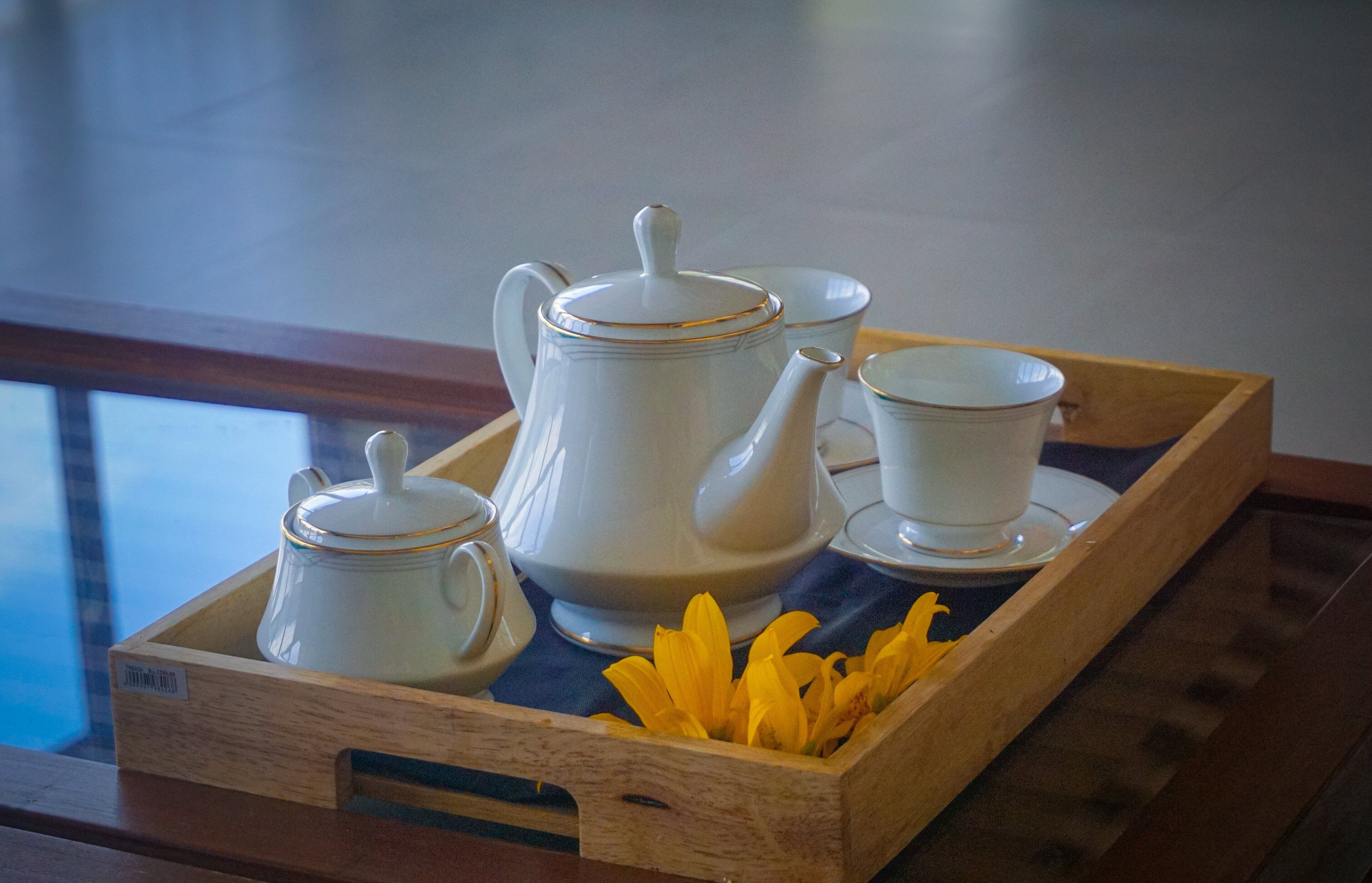 A tray with a teapot, cups, and saucers, accompanied by yellow flowers.