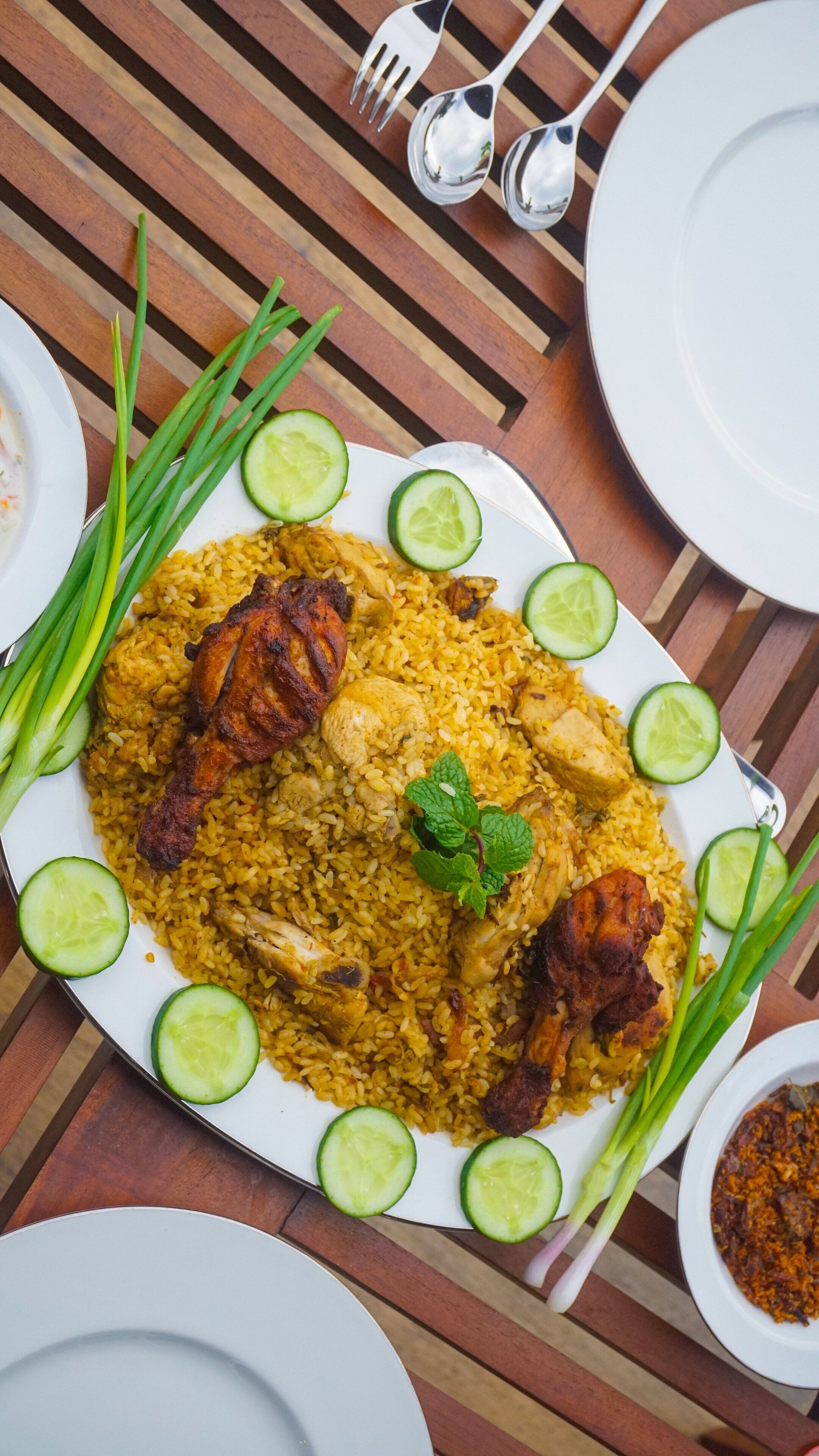 A plate of yellow rice with chicken pieces and cucumber slices on a wooden table.