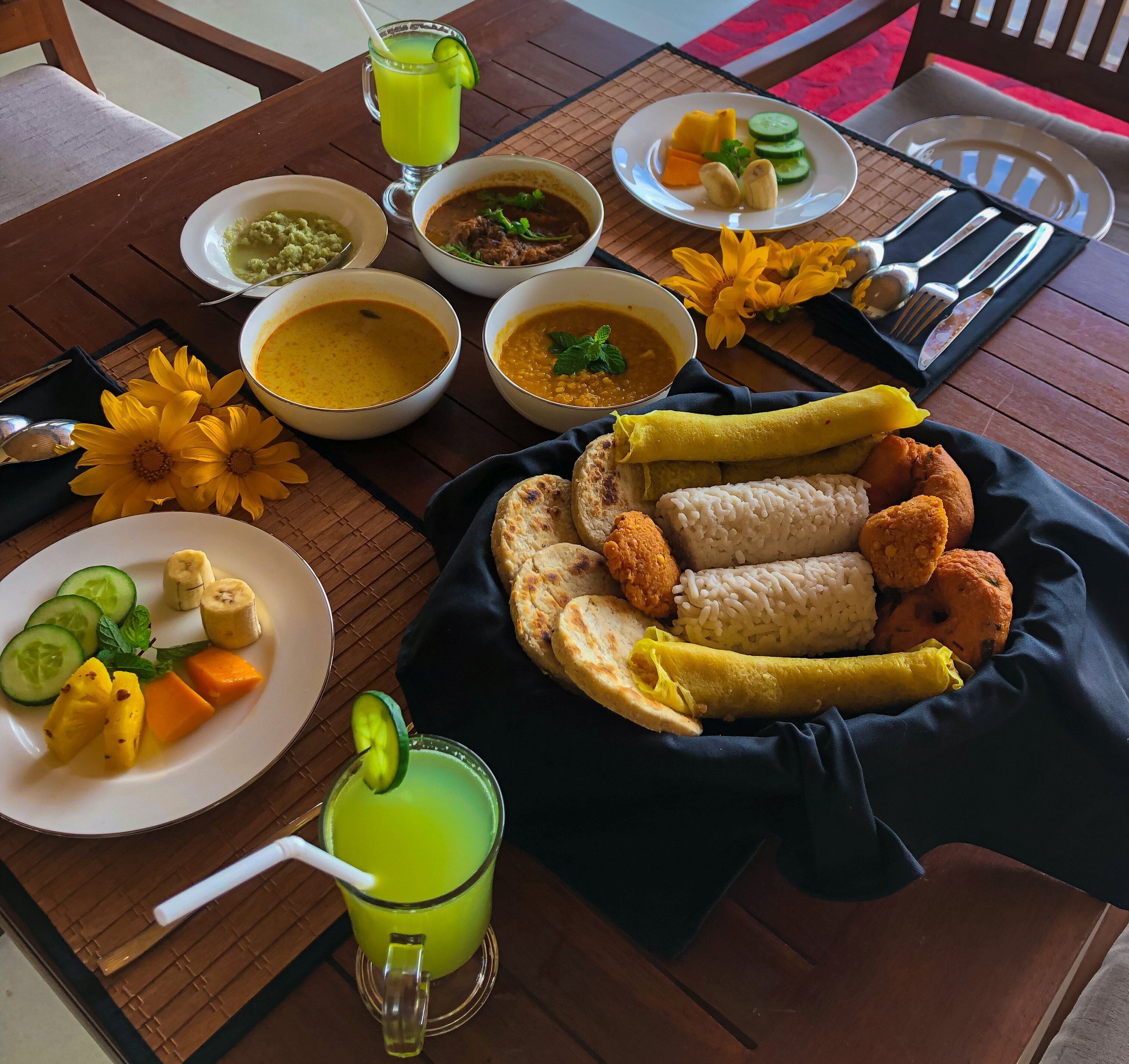 A table with various dishes including bowls of soup, a plate with sliced vegetables, and a plate with fried items.
