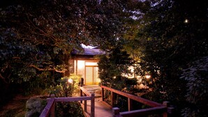A wooden pathway leading to a traditional Japanese gate, surrounded by dense foliage and illuminated by soft lighting. - Hotel Parens Onoya (Asakura)