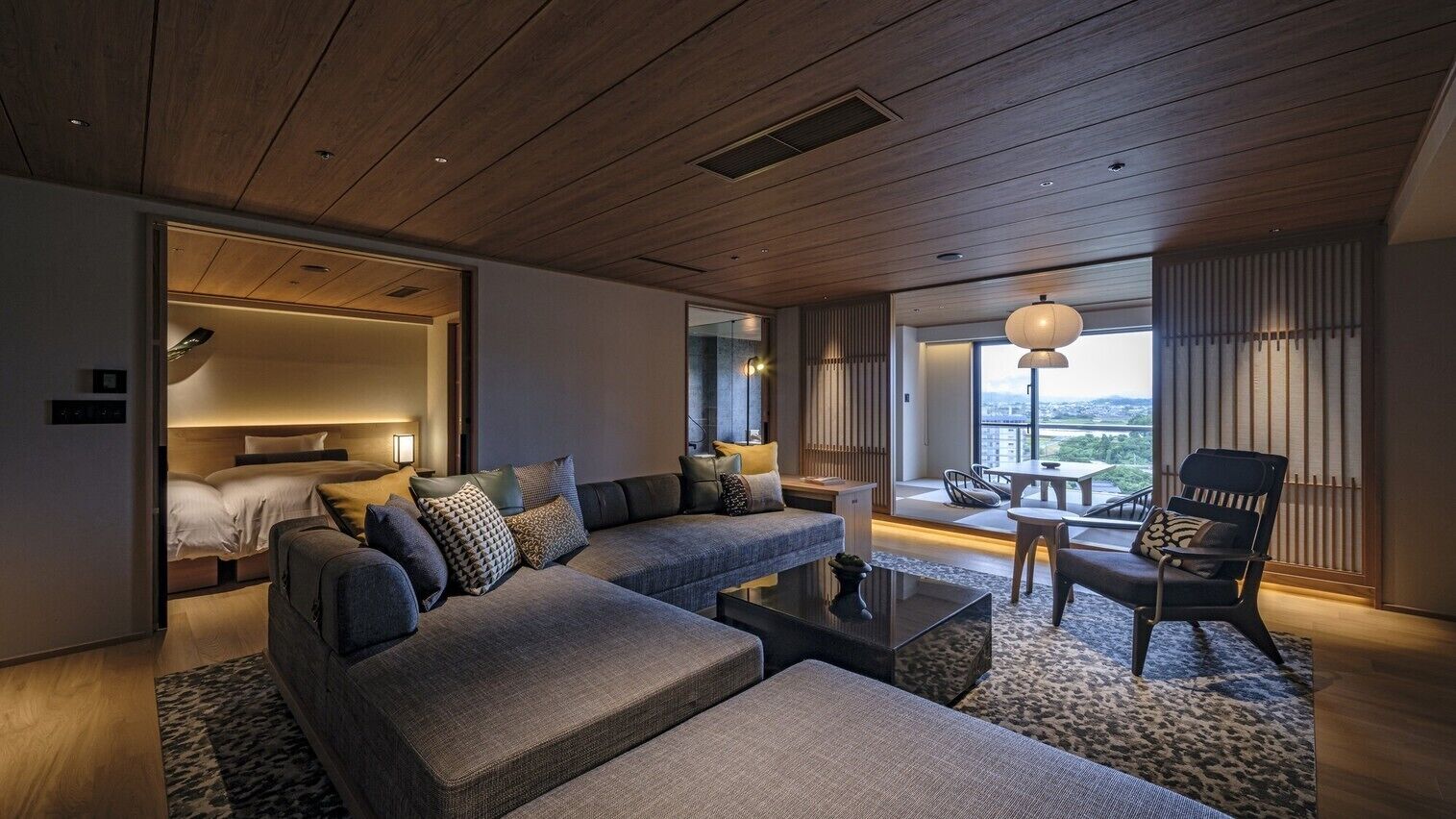 Habitación de hotel moderna con un sofá grande, una mesa de centro, una silla, una cama y vistas a la ciudad.