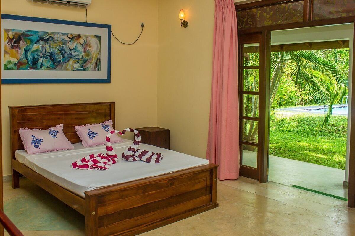 Un dormitorio con una cama de madera, un cuadro en la pared y vistas a un jardín verde a través de un ventanal.