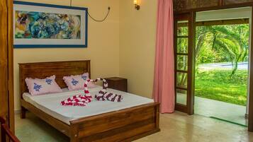 A bedroom with a wooden bed, a painting on the wall, and a view of a green garden through a glass door.