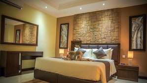 Un dormitorio moderno con una pared de acento de piedra, una cama grande con cabecera, una mesita de noche con lámpara y un espejo amplio.
