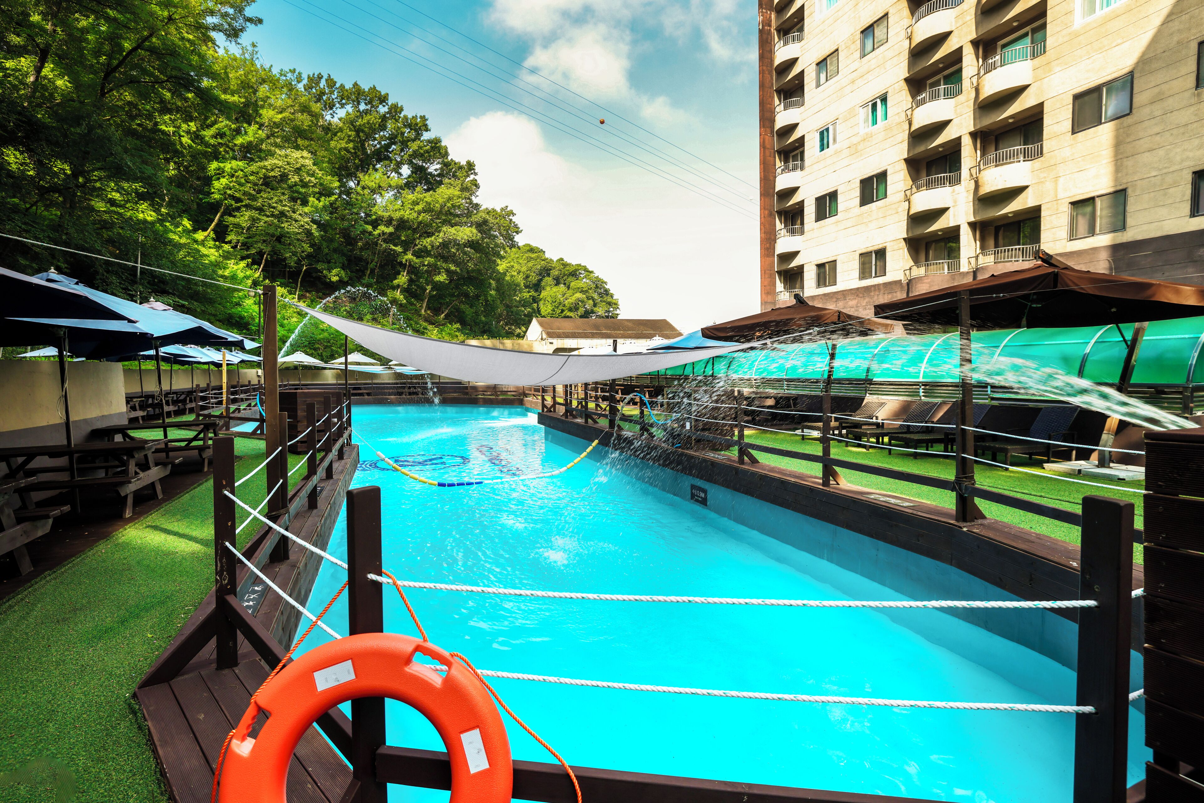 A swimming pool with a wooden deck, safety equipment, and umbrellas.