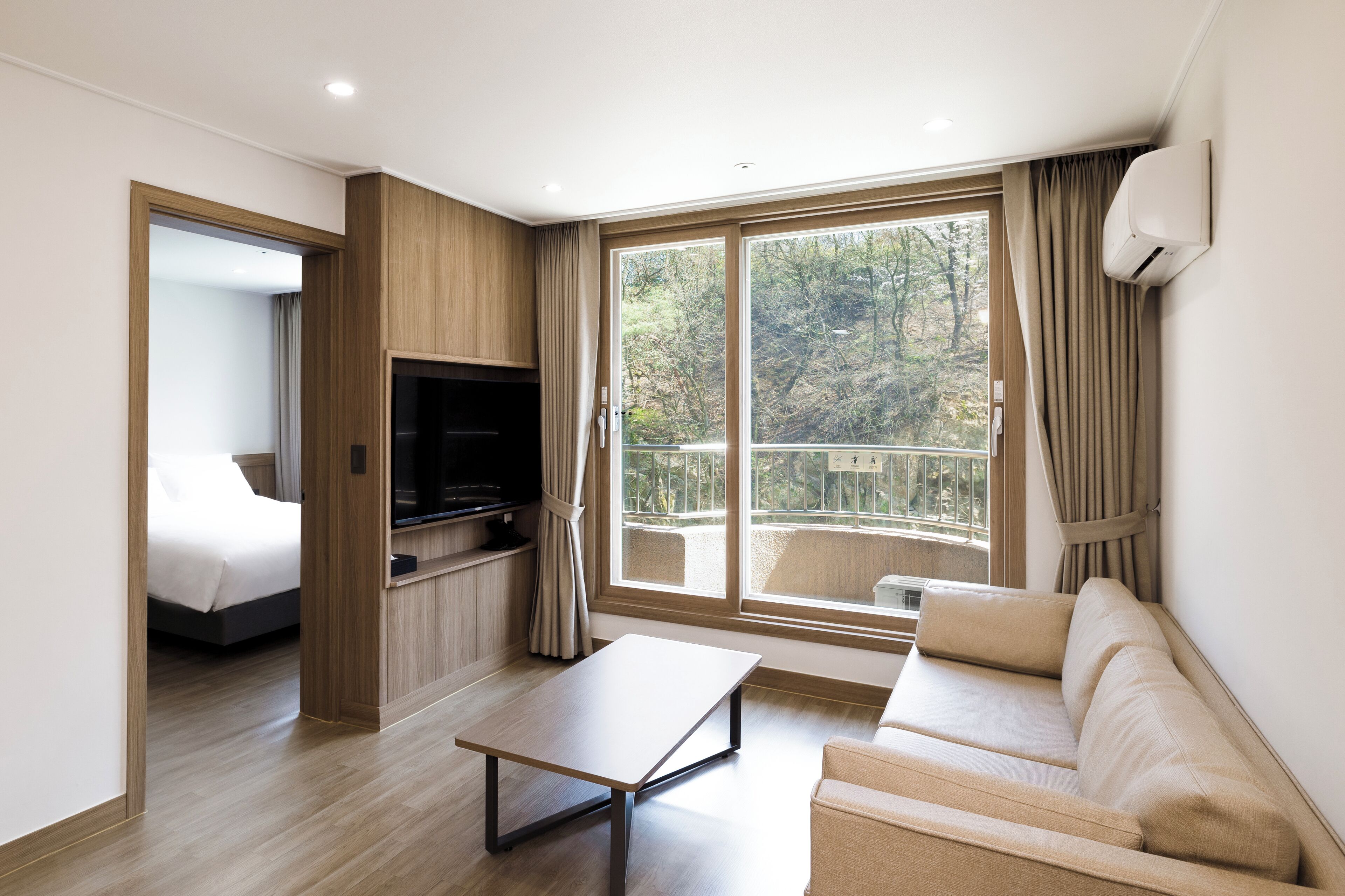 A modern living room with a sofa, a coffee table, a TV, and a balcony with curtains.
