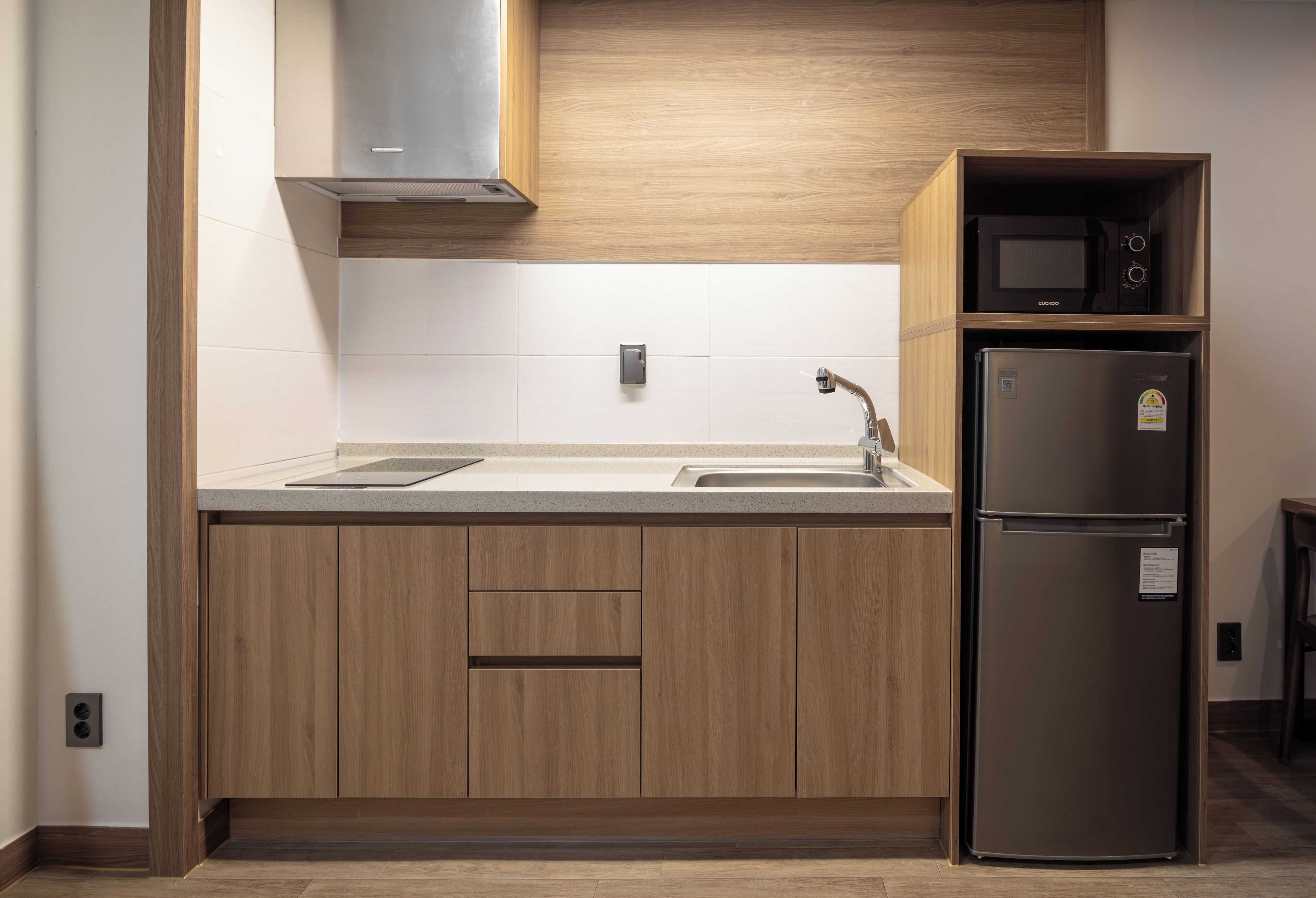 A modern kitchen with wooden cabinets, a stainless steel sink, a microwave, and a refrigerator.