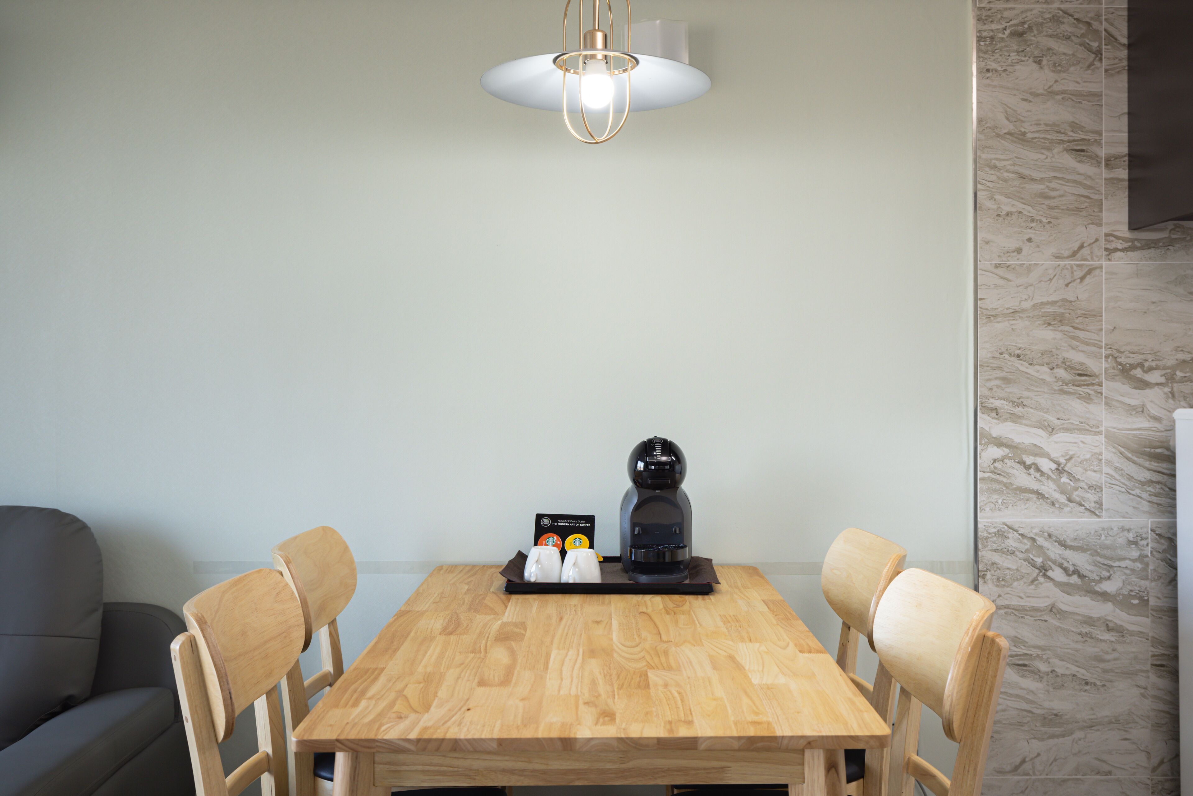 Un comedor con una mesa de madera, cuatro sillas, una cafetera y una lámpara.