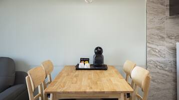 Un comedor con una mesa de madera, cuatro sillas, una cafetera y una lámpara.