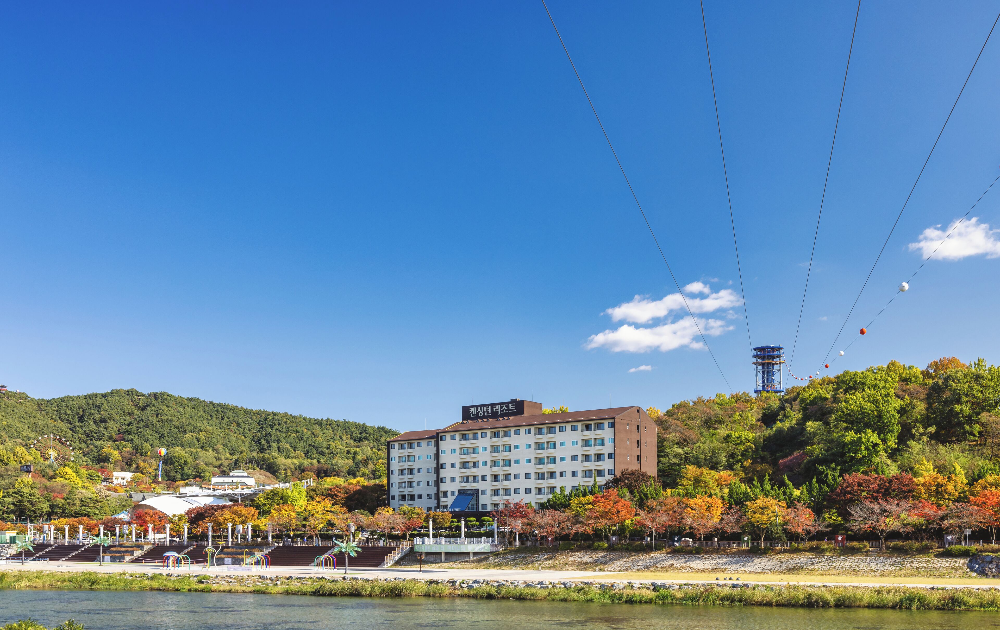 A hotel with a modern design, located near a body of water and surrounded by autumn foliage.