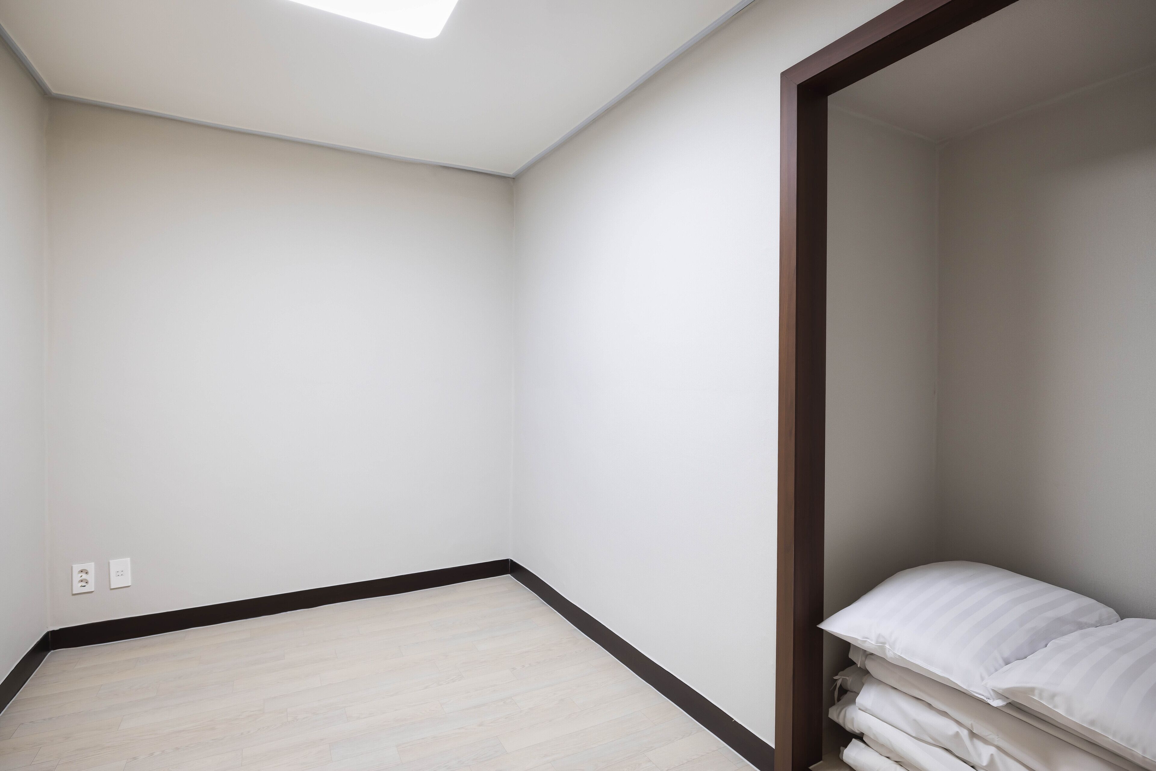 A room with a sloped ceiling, a light wooden floor, and a corner bed with white bedding.