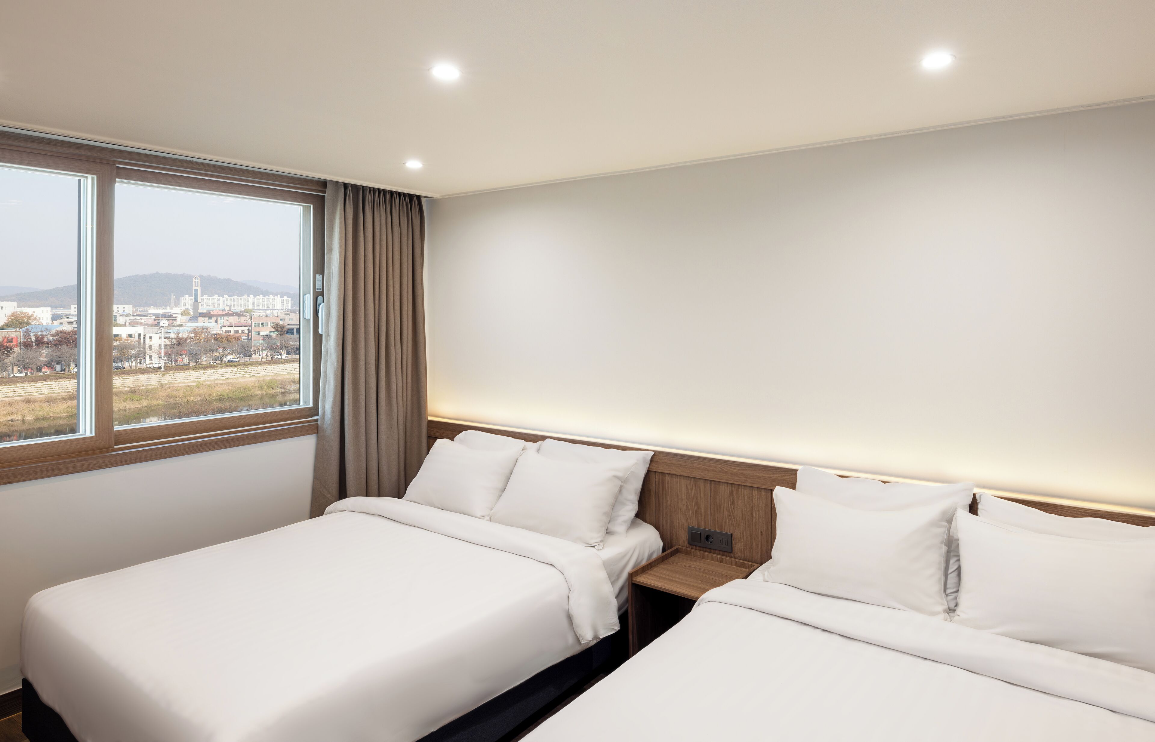 Habitació d'hotel amb dos llits, un finestral gran i vista a la ciutat.