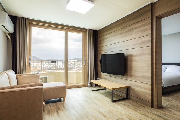 A modern hotel room with a large window, a flat-screen TV, a sofa, and a bed.
