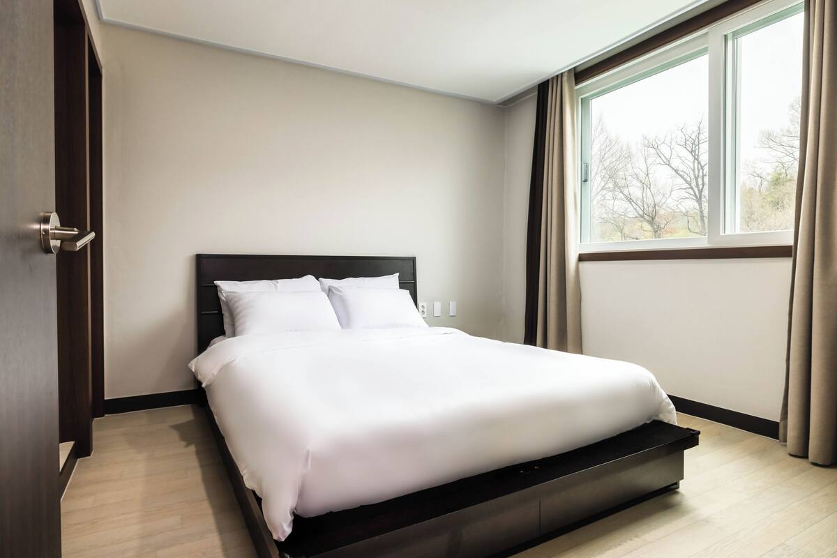 Une chambre d’hôtel moderne avec un grand lit, une fenêtre avec des rideaux et un plancher en bois.
