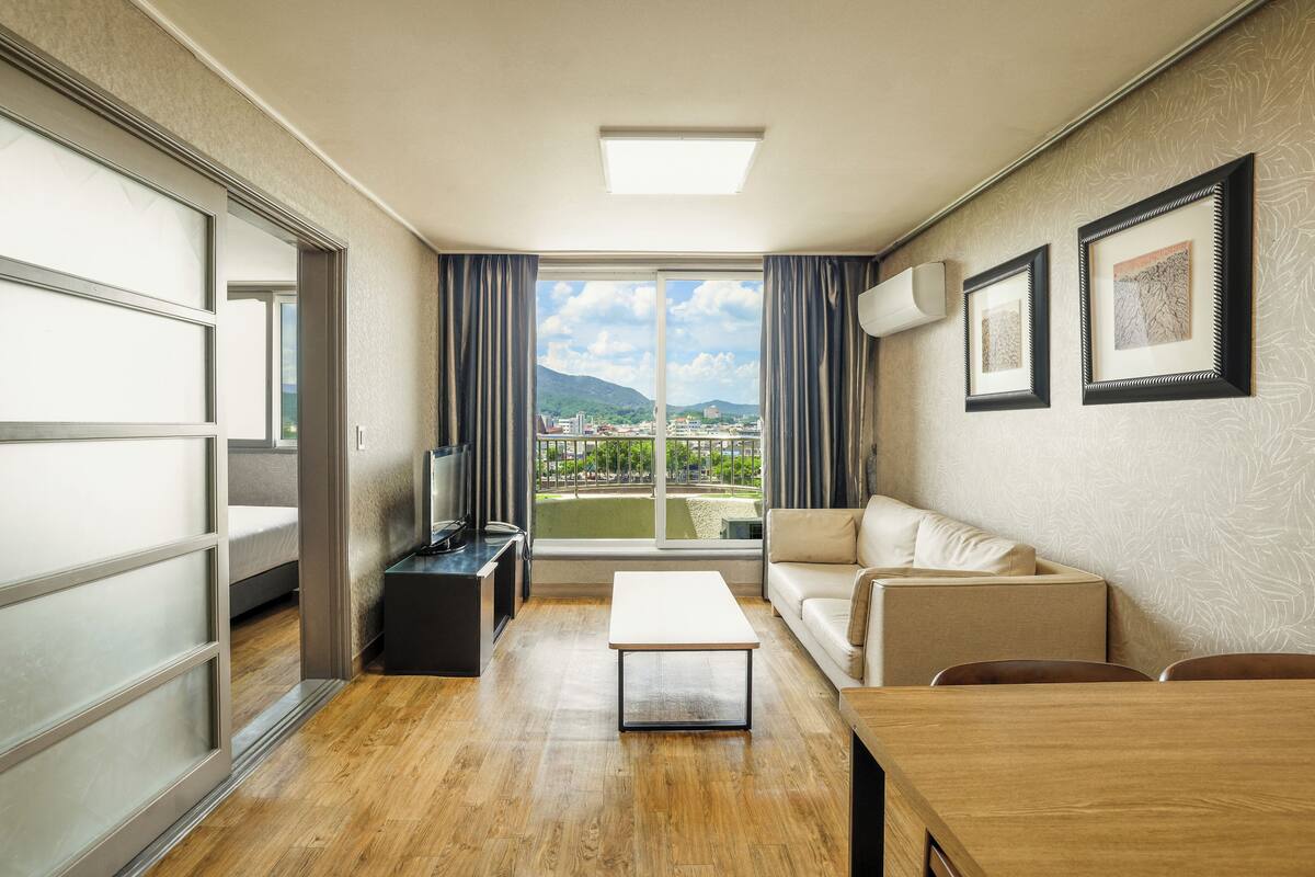 Une chambre d’hôtel moderne, dotée d’un canapé, d’une table basse, d ’un téléviseur et offrant une vue sur le paysage urbain grâce à de grandes fenêtres.