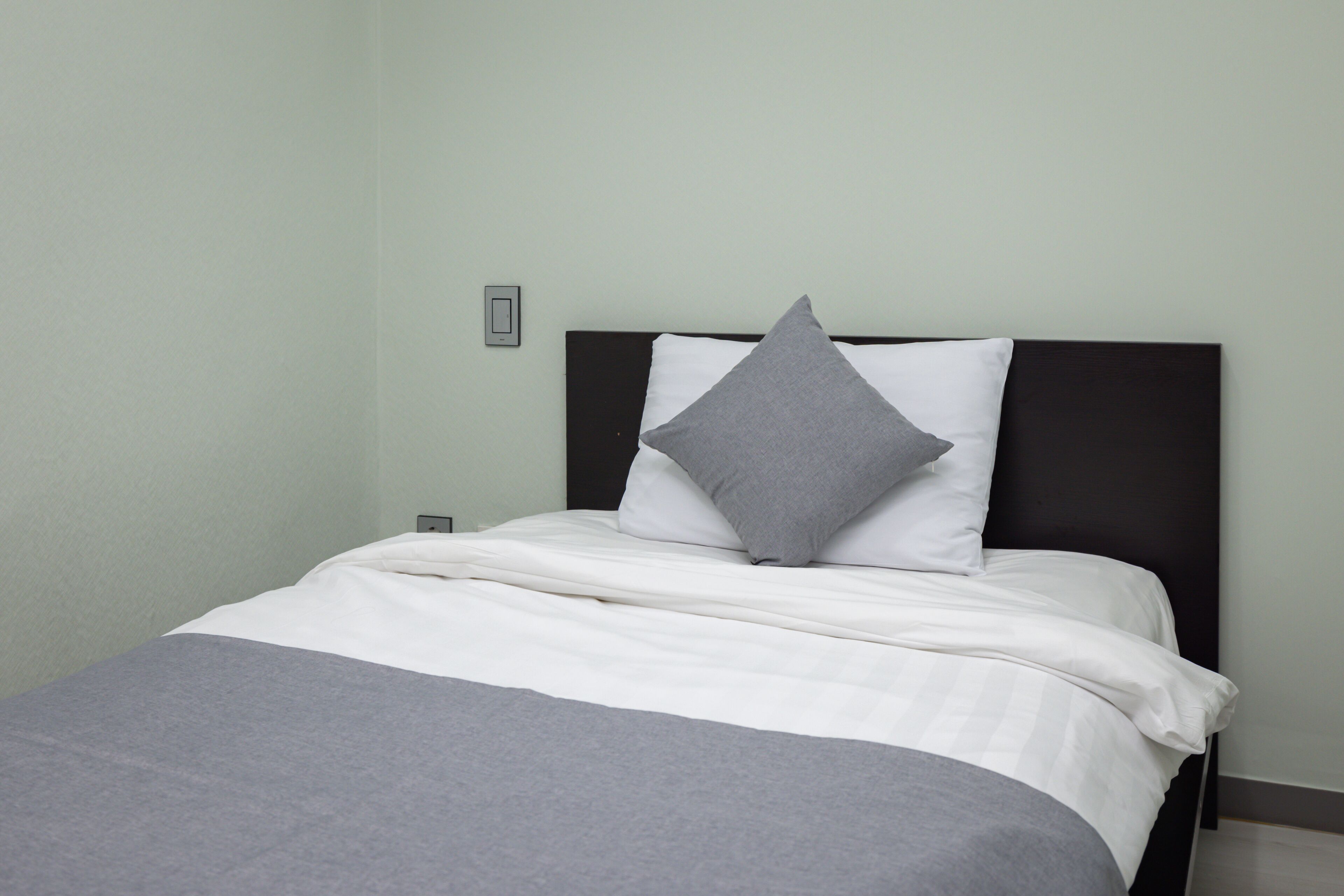 A neatly made bed with white and gray bedding, a dark headboard, and a light-colored wall.
