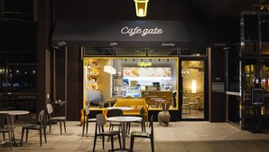 Une devanture de magasin « Cafe Gate » avec un intérieur de café, des places assises en plein air et un panneau lumineux au néon.