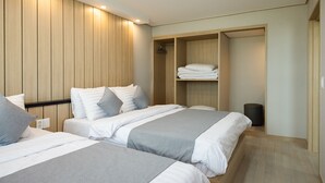 Une chambre d’hôtel moderne avec deux lits, une armoire en bois et une petite poubelle.