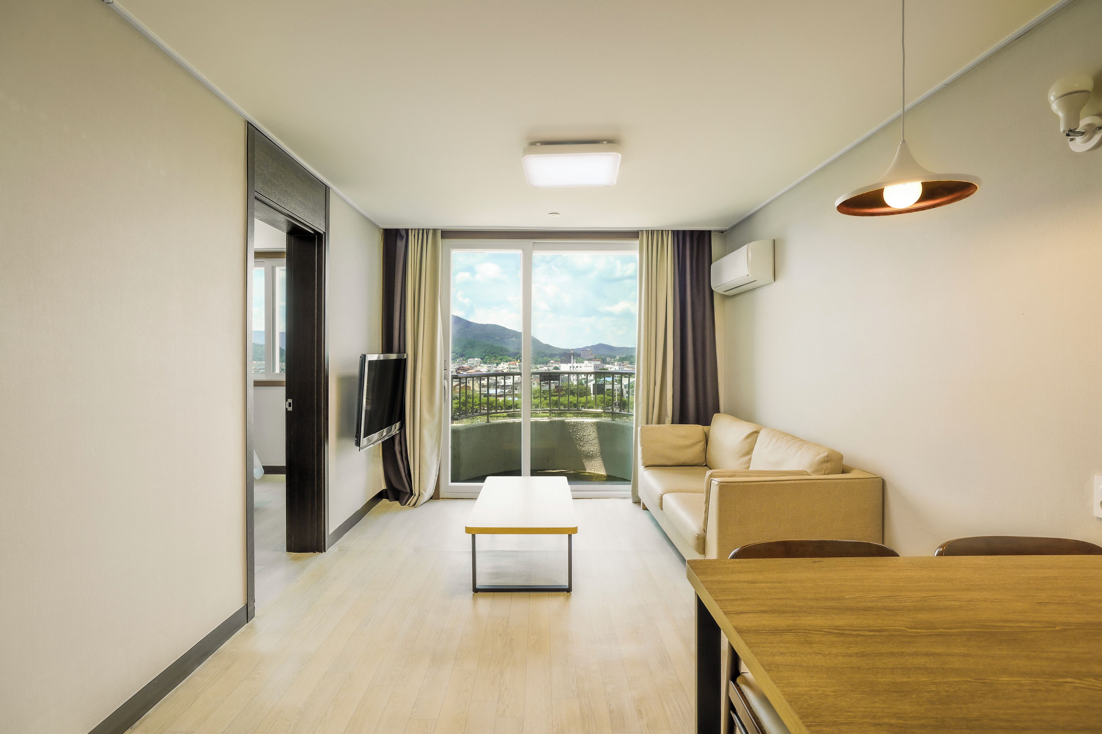 Un salon moderne avec un canapé, une table basse et une table à manger. Une grande fenêtre offre une vue sur le paysage urbain et les montagnes.