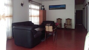 A living room with a dark sofa, two wooden chairs, a wooden cabinet, and a ceiling fan. - Mia's Villa (Hikkaduwa)