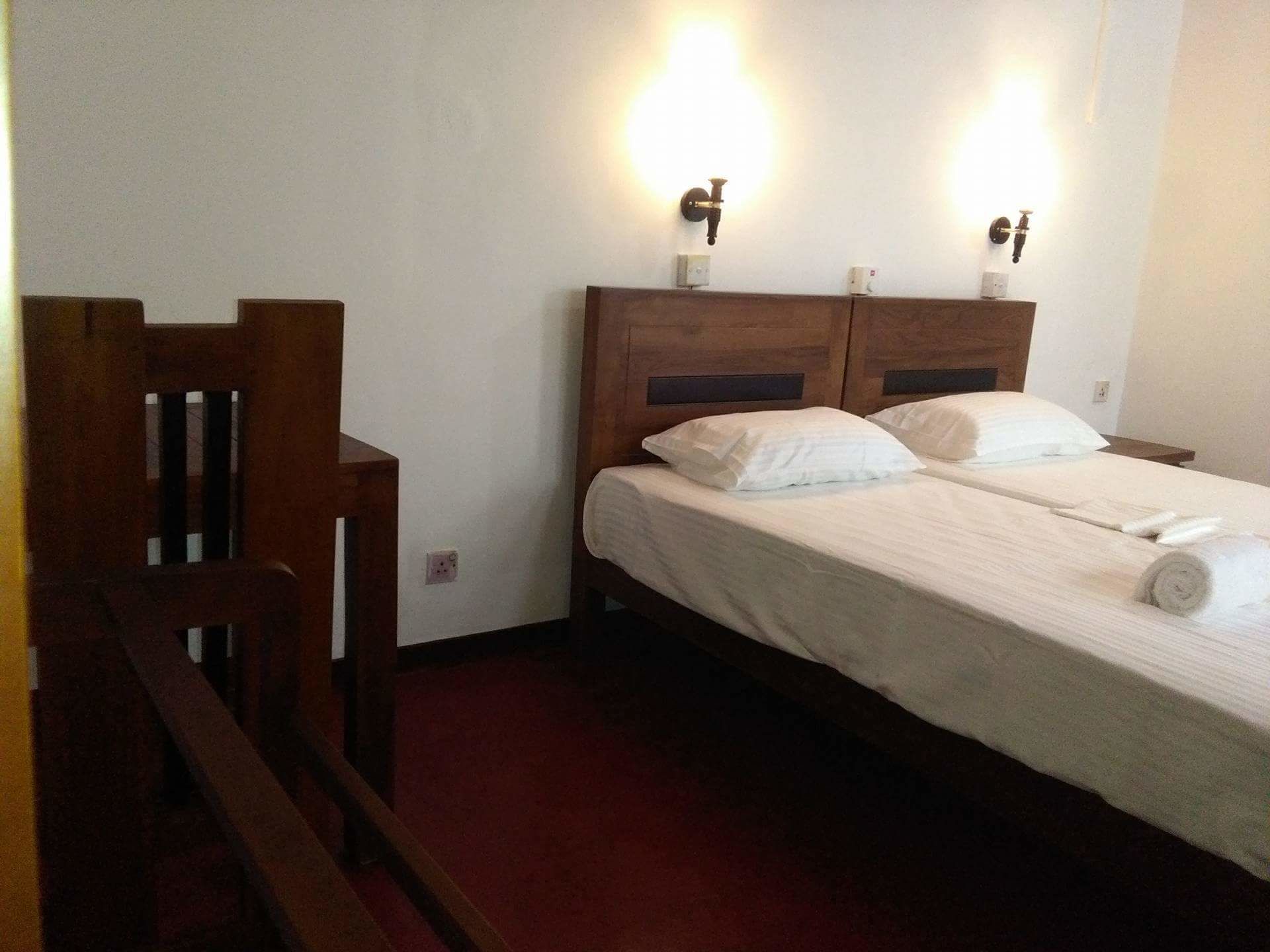 Habitación de hotel con dos camas individuales, cabeceros de madera y luces fijadas a la pared.