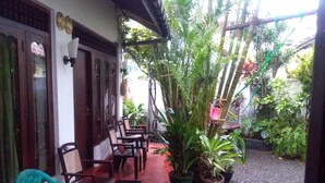 A covered outdoor seating area with wooden chairs and tables, surrounded by potted plants and a gravel path. - Mia's Villa (Hikkaduwa)