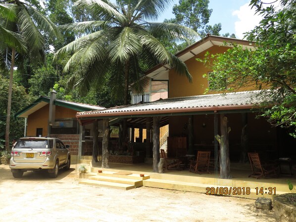 A two-story building with a covered porch, a car parked in front, and palm trees in the background.