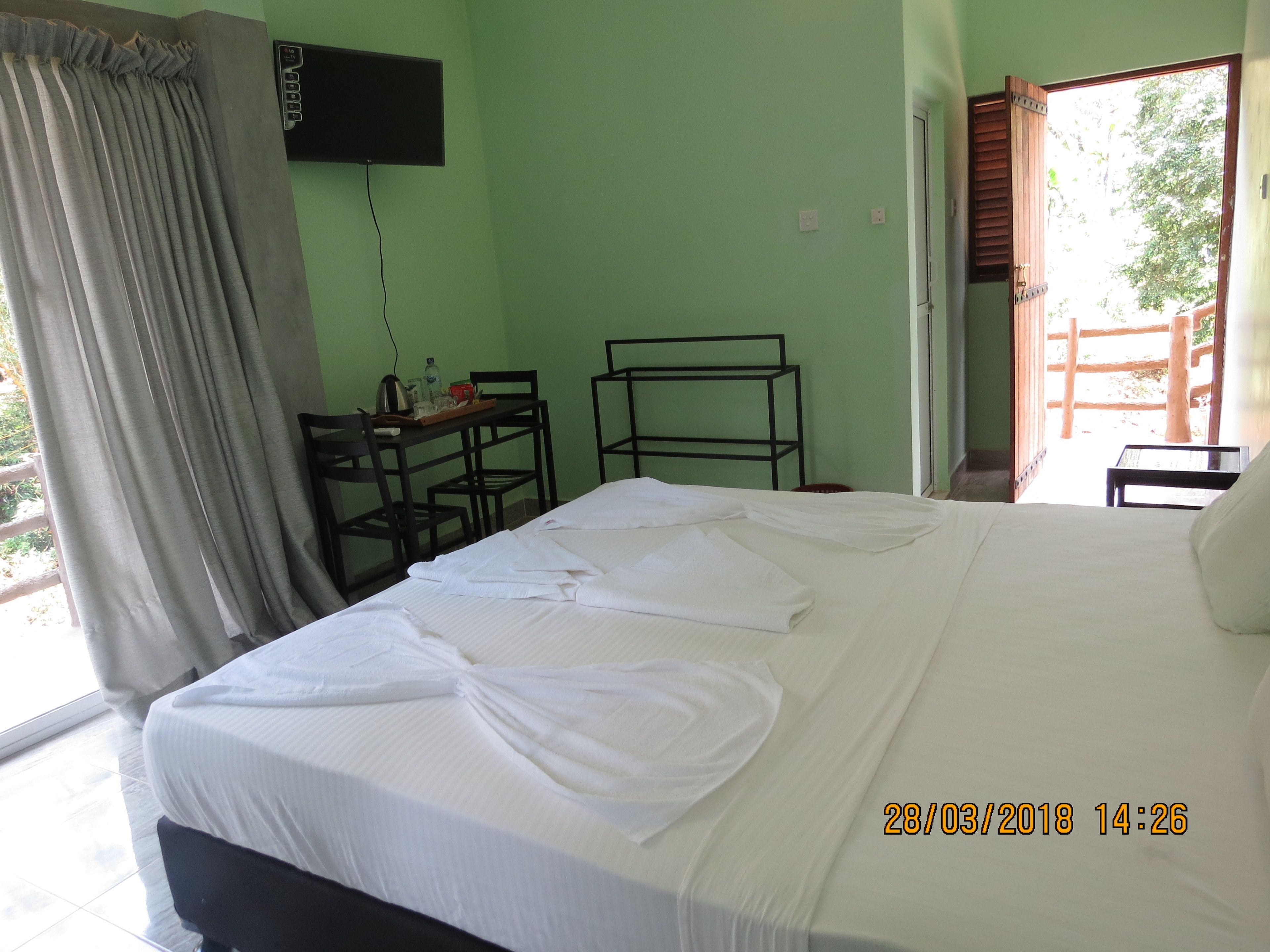 A hotel room with a bed, a desk, a chair, a TV, and a view of the outside.