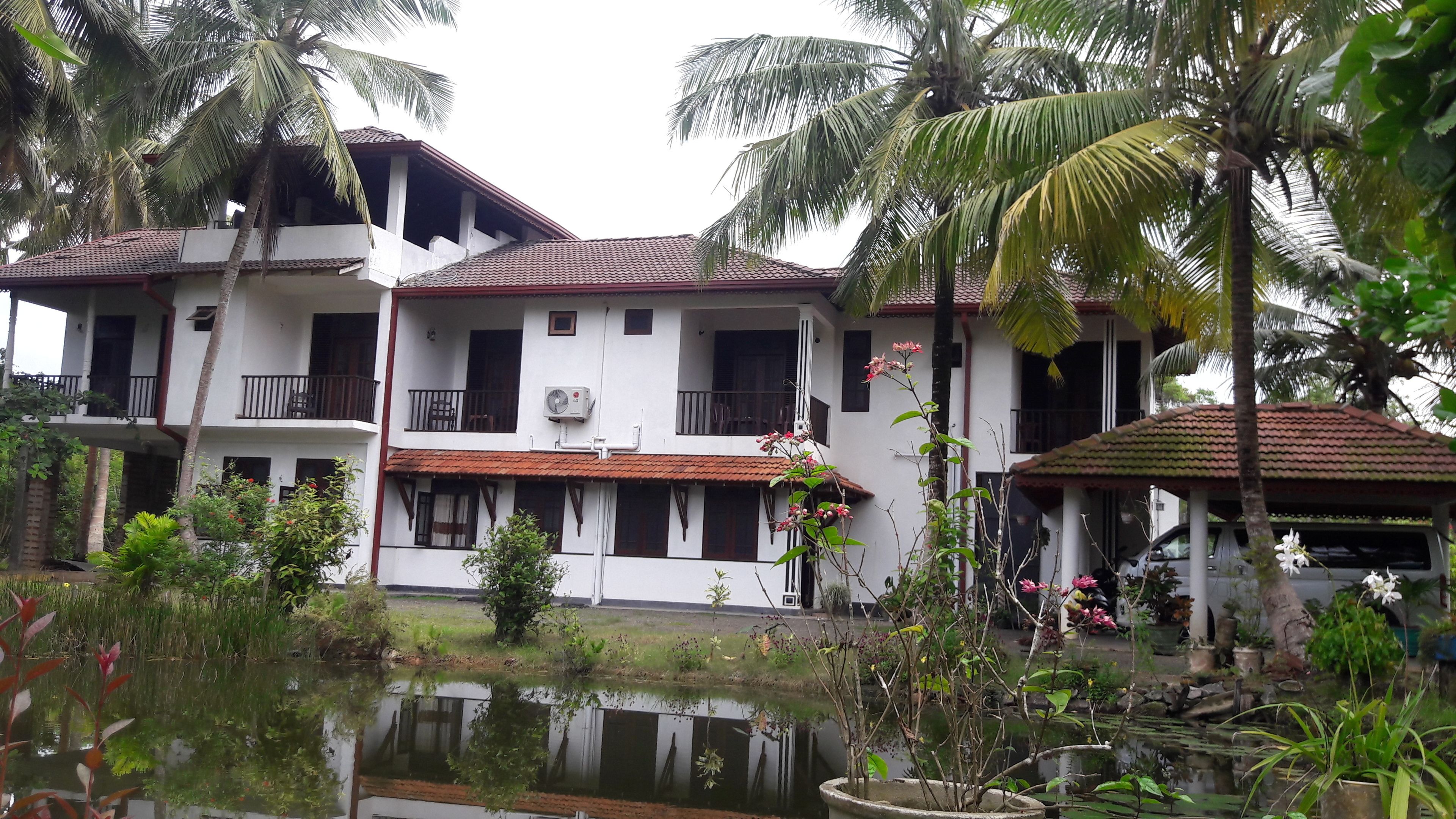 A two-story building with a tiled roof, a balcony, and a water feature in front.