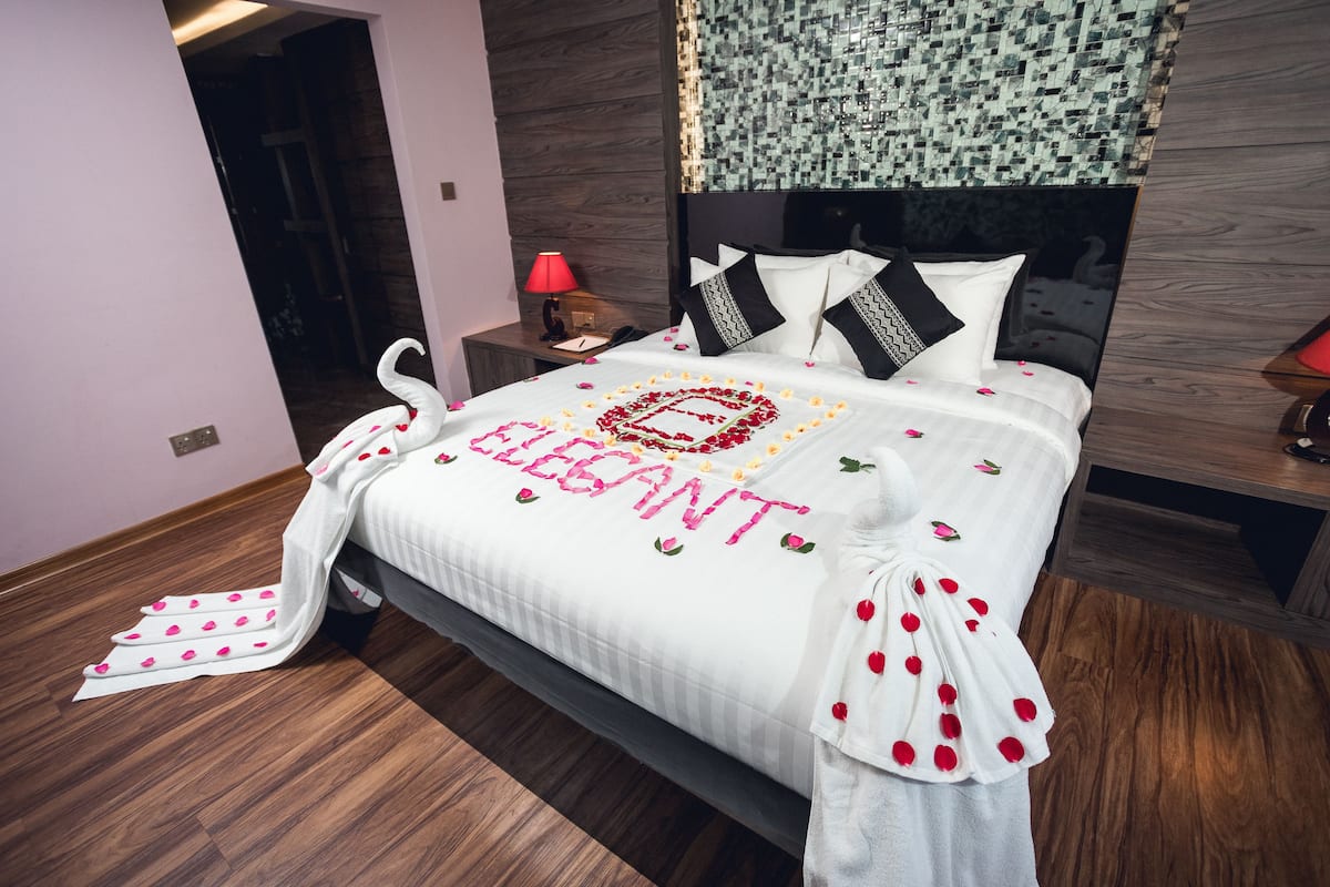 A neatly made bed with a white bedspread and a decorative heart-shaped arrangement of flowers spelling "ELEGANT."