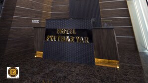 En moderne hotellobby med en markant receptionsdisk, et stort logo og en trappe op til et højere niveau.