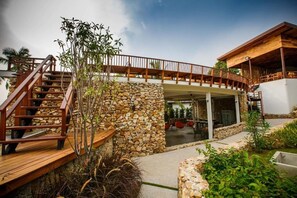Un bâtiment moderne doté d’un mur en pierre, d’une terrasse en bois et d’un espace extérieur couvert aménagé avec des sièges.