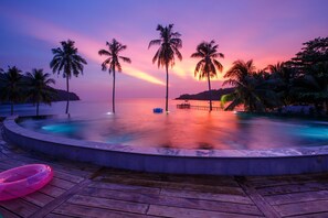 A pool area with a wooden deck, palm trees, and a sunset view.