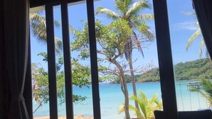 Une pièce dotée de grandes fenêtres donnant sur une plage et des palmiers.