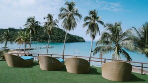 Un salon de plage doté de fauteuils en osier et offrant une vue sur la mer et un quai.