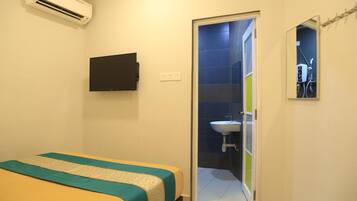 Una habitación con cama, televisor de pantalla plana, aire acondicionado, baño con lavamanos y espejo, y una puerta que da a otra habitación.